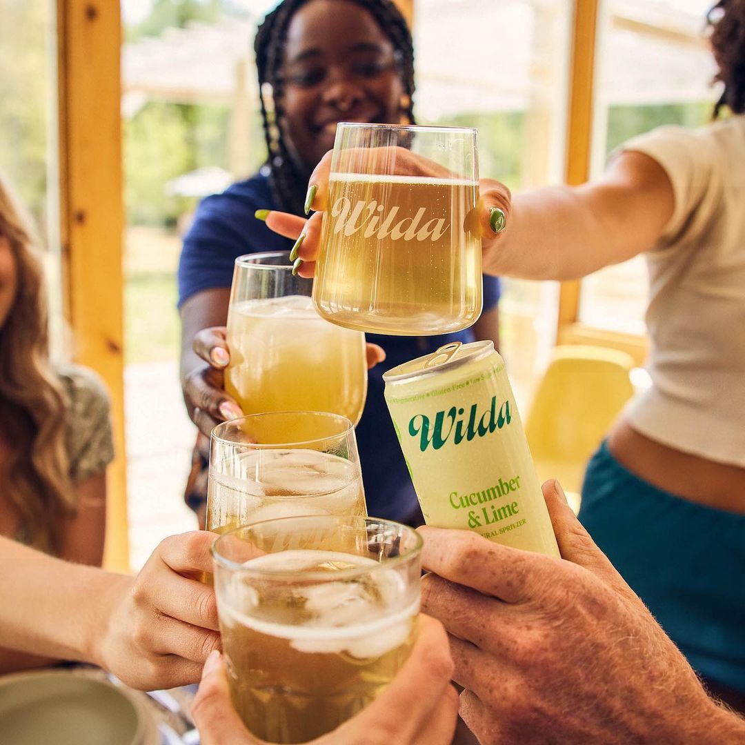 Group toasting with glasses and a can of cucumber lime drink, bright and cheerful gathering with friends, enjoying beverages together.