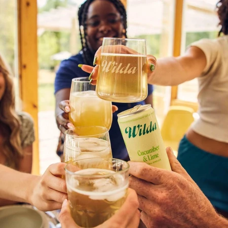 Group toasting with glasses and a can of cucumber lime drink, bright and cheerful gathering with friends, enjoying beverages together.