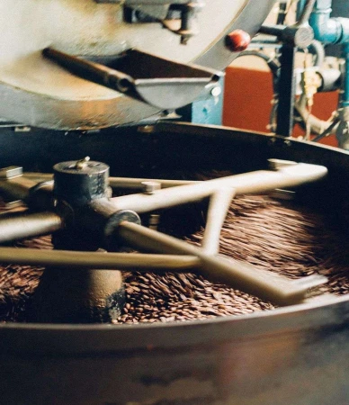 Coffee beans roasting in an industrial machine, showcasing the roasting process, the metallic machinery, and the rich, dark color of the beans.