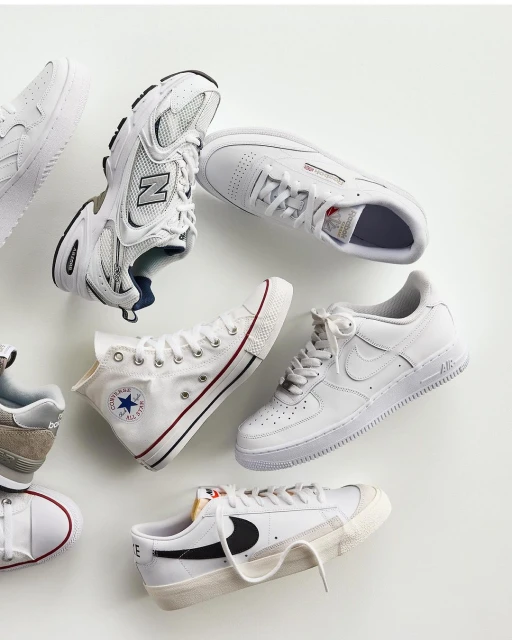 Collection of athletic shoes in white and neutral tones including sneakers and canvas trainers, artfully arranged on a light background.