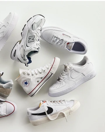 Collection of athletic shoes in white and neutral tones including sneakers and canvas trainers, artfully arranged on a light background.
