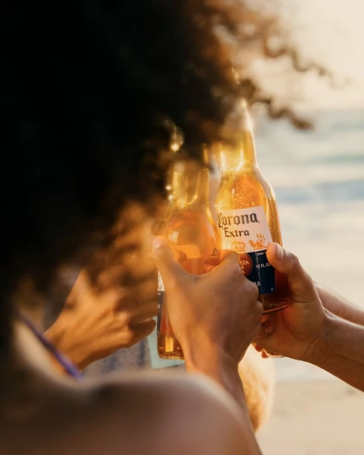Group of friends toasting Corona Extra beers at the beach during sunset, creating a summery, social, and refreshing vibe.