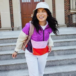 Smiling woman wearing a bucket hat and colour block windbreaker walking down stone steps outdoors in Chicago