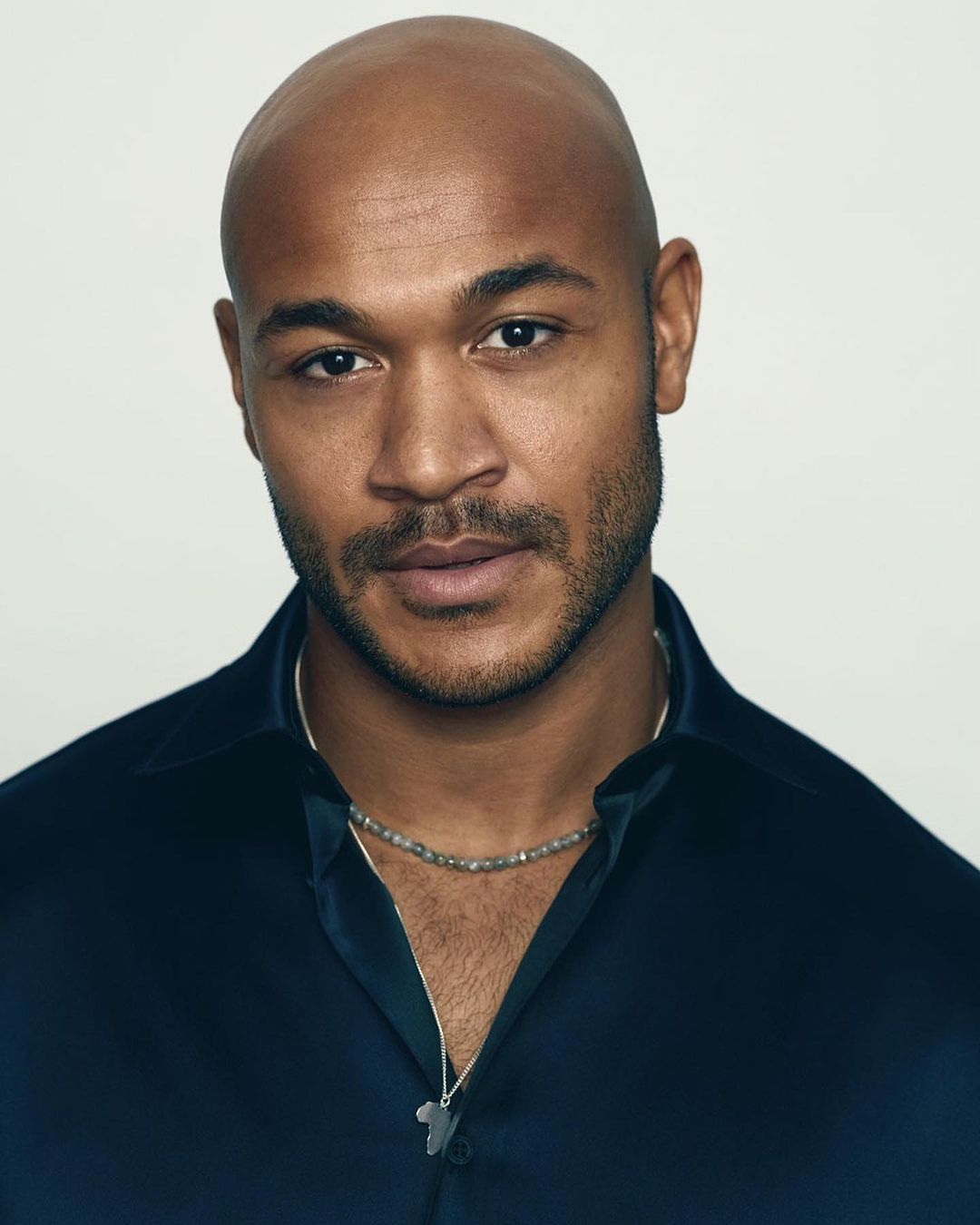 Close-up portrait of a bald black man wearing a dark blue shirt and beaded necklace by photographer Ralph Mecke.