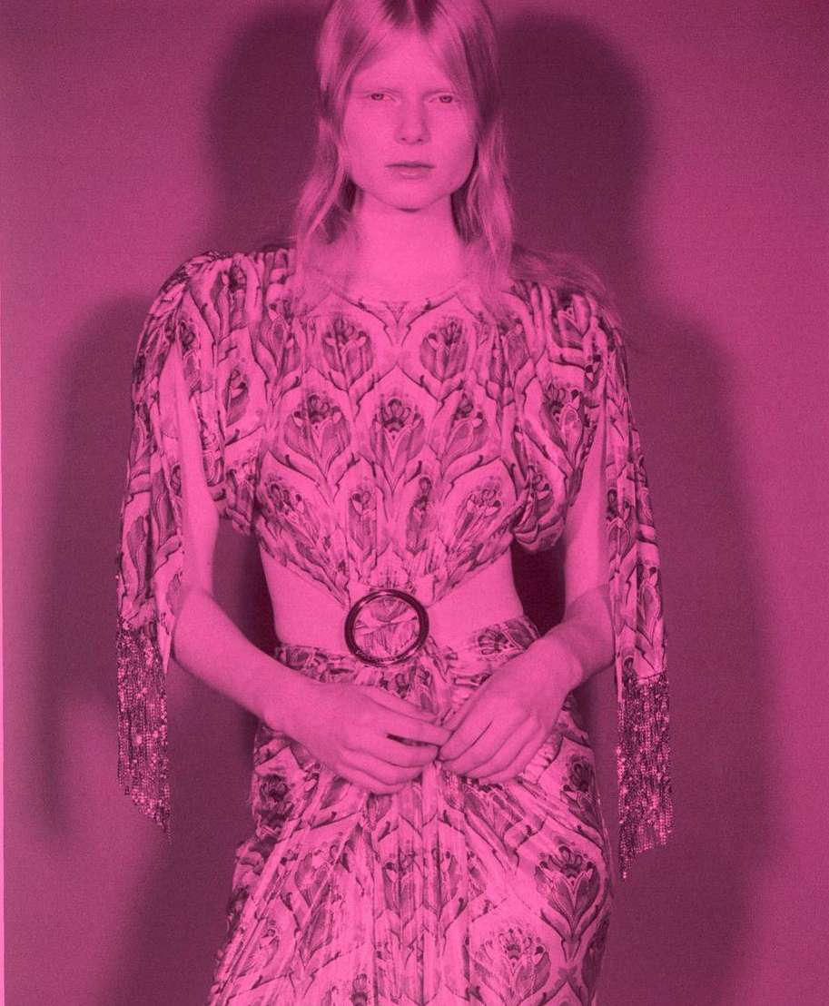Adult woman poses wearing a patterned dress with belt on a pink background in a studio shot. Fashion and portrait photography.