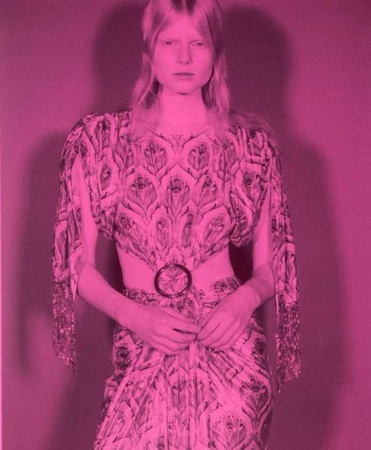 Adult woman poses wearing a patterned dress with belt on a pink background in a studio shot. Fashion and portrait photography.