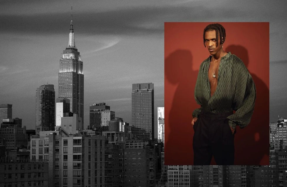 Portrait of a male model wearing an open green shirt against a cityscape featuring the Empire State Building in the background.