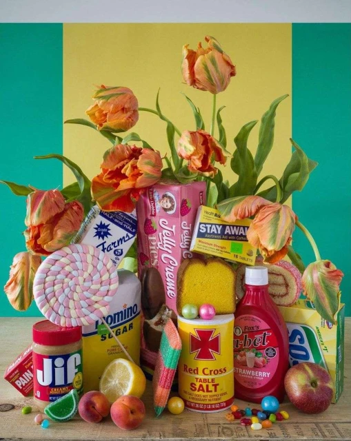 Still life arrangement of colorful tulips, candies, and food packaging against a yellow and green background in a studio setting.