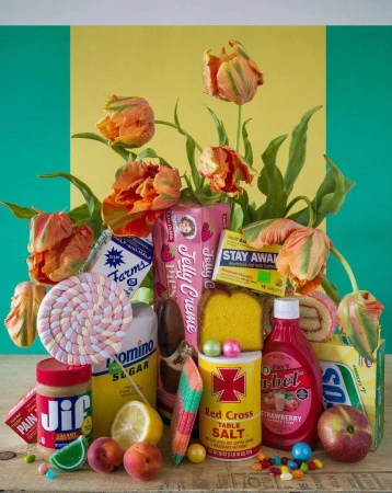 Still life arrangement of colorful tulips, candies, and food packaging against a yellow and green background in a studio setting.