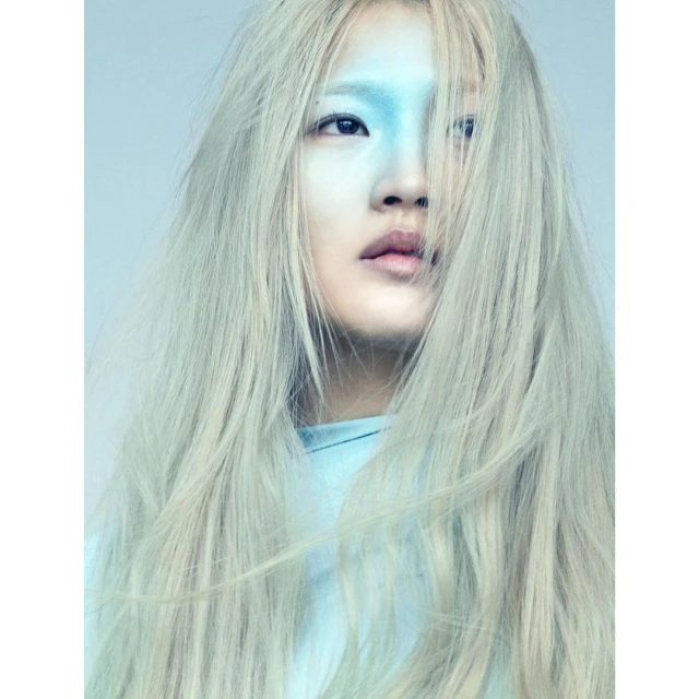 Portrait of an adult female with fair skin and long white hair posing indoors with her face painted blue in an eye-level shot.