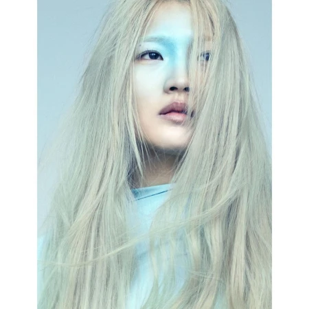 Portrait of an adult female with fair skin and long white hair posing indoors with her face painted blue in an eye-level shot.