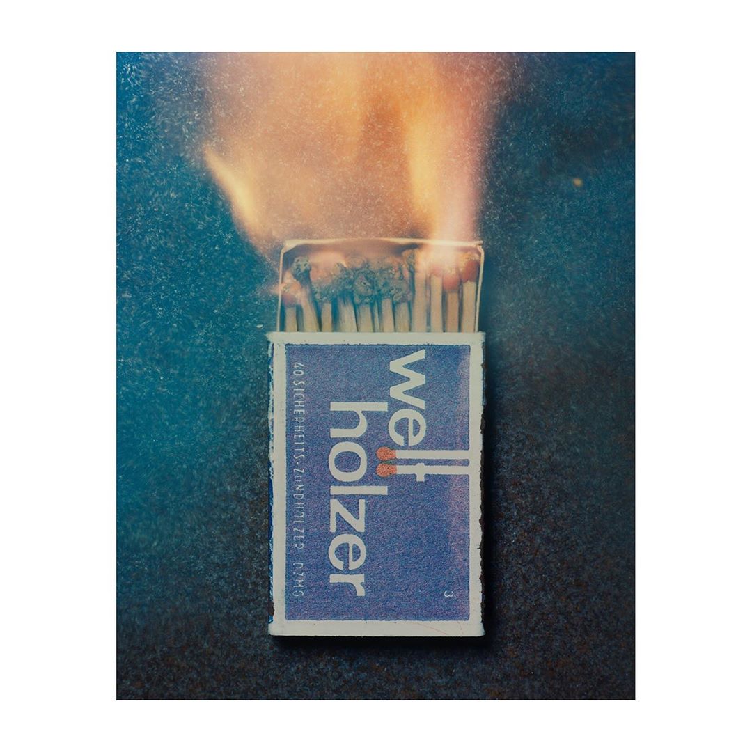 Close-up photograph of an open box of matches with lit match heads, a vintage aesthetic with blue and orange color grading.