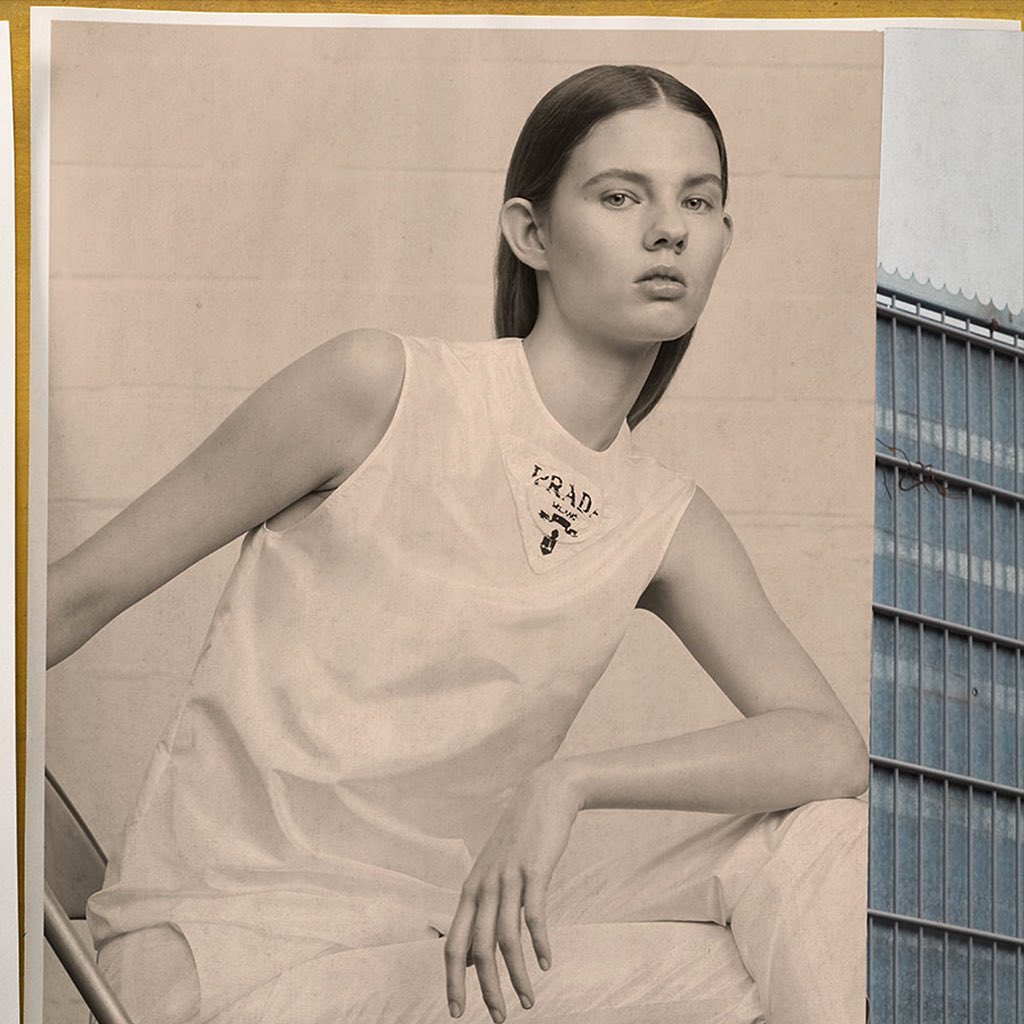 Fashion editorial photograph of an adult woman in white clothing with 'PRADA' logo, posed against an indoor and outdoor backdrop.