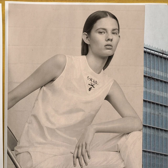Fashion editorial photograph of an adult woman in white clothing with 'PRADA' logo, posed against an indoor and outdoor backdrop.