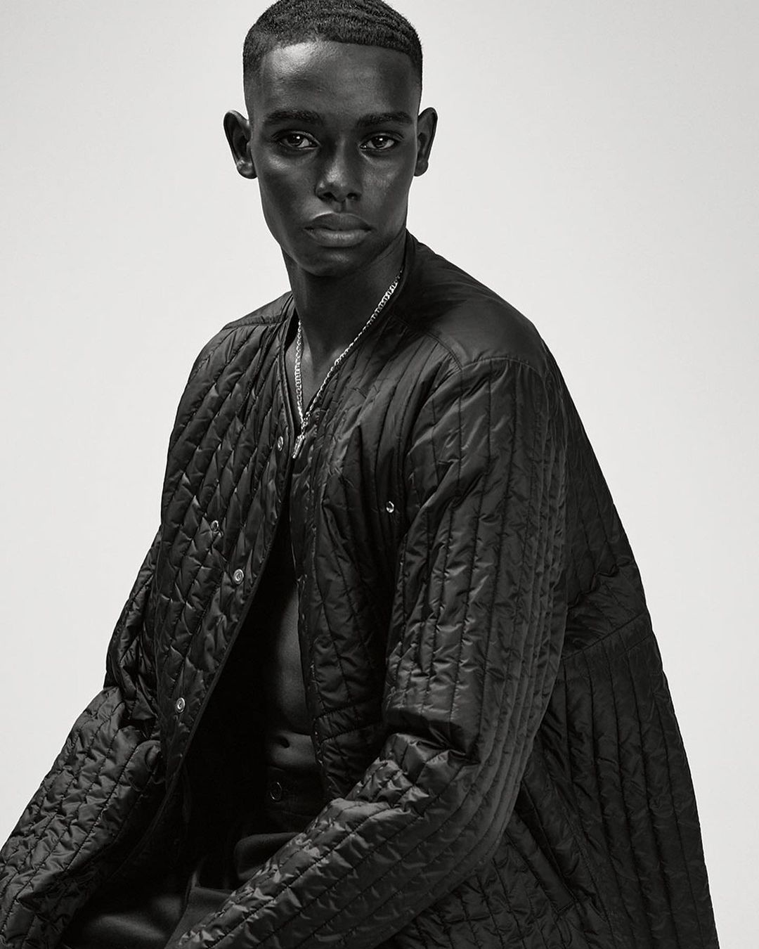 Portrait of a Black man wearing a black quilted jacket against a plain white background by Ralph Mecke