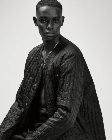 Portrait of a Black man wearing a black quilted jacket against a plain white background by Ralph Mecke