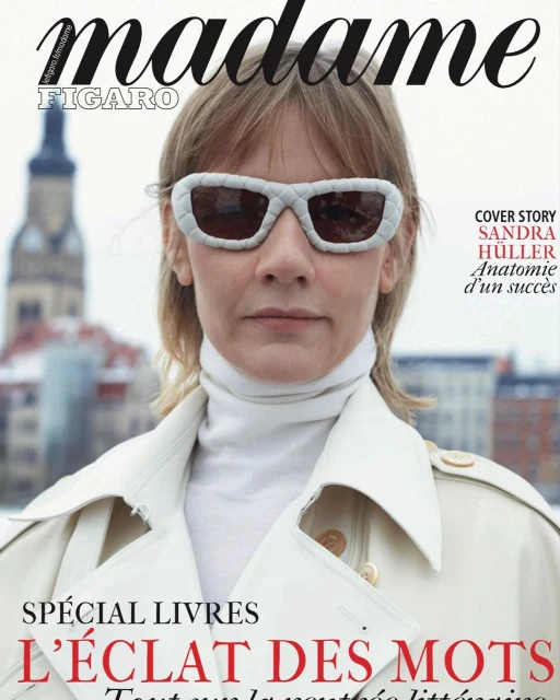 Fashion magazine cover featuring Sandra Huller wearing white sunglasses and coat, with a blurred cityscape background and magazine text.