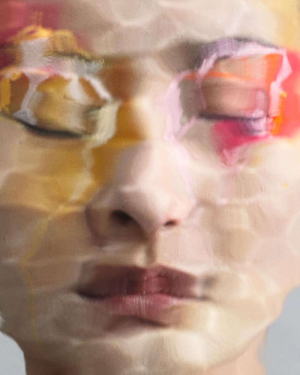 Artistic close-up of a person's face with closed eyes, showcasing a watercolor effect with dominant colors of yellow, pink, and white.