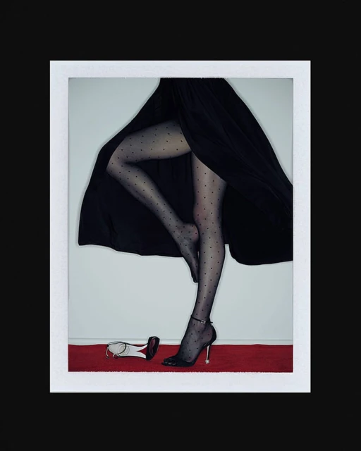 Elegant studio shot of a woman's legs in dotted stockings and black heels on a red carpet, with a matching shoe lying beside her.