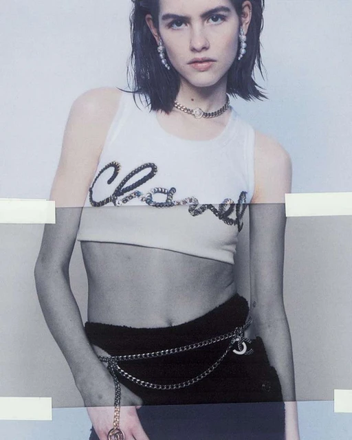 Female fashion model poses wearing a Chanel tank top and chain belt, accessorized with a necklace and pearl earrings in a studio shot.