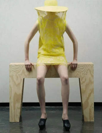 Model wearing yellow dress and veiled hat sitting on wooden bench by photographer Ralph Mecke