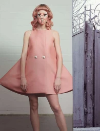 Model in pink A-line dress with elaborate prosthetic facial art against a brick wall, photographed by Ralph Mecke