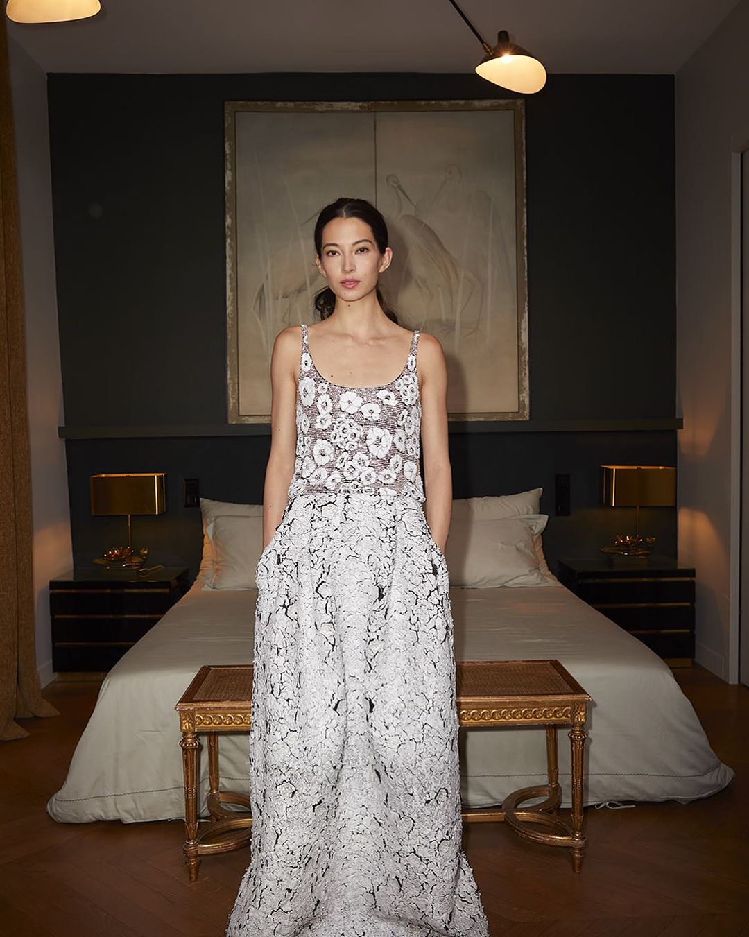 Model standing in a bedroom wearing a patterned white floral sleeveless top and matching patterned maxi skirt by photographer Ralph Wenig.