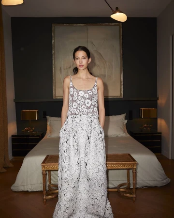 Model standing in a bedroom wearing a patterned white floral sleeveless top and matching patterned maxi skirt by photographer Ralph Wenig.