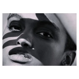 Close-up black and white portrait of a person with strong diagonal shadow lines cast across the face.