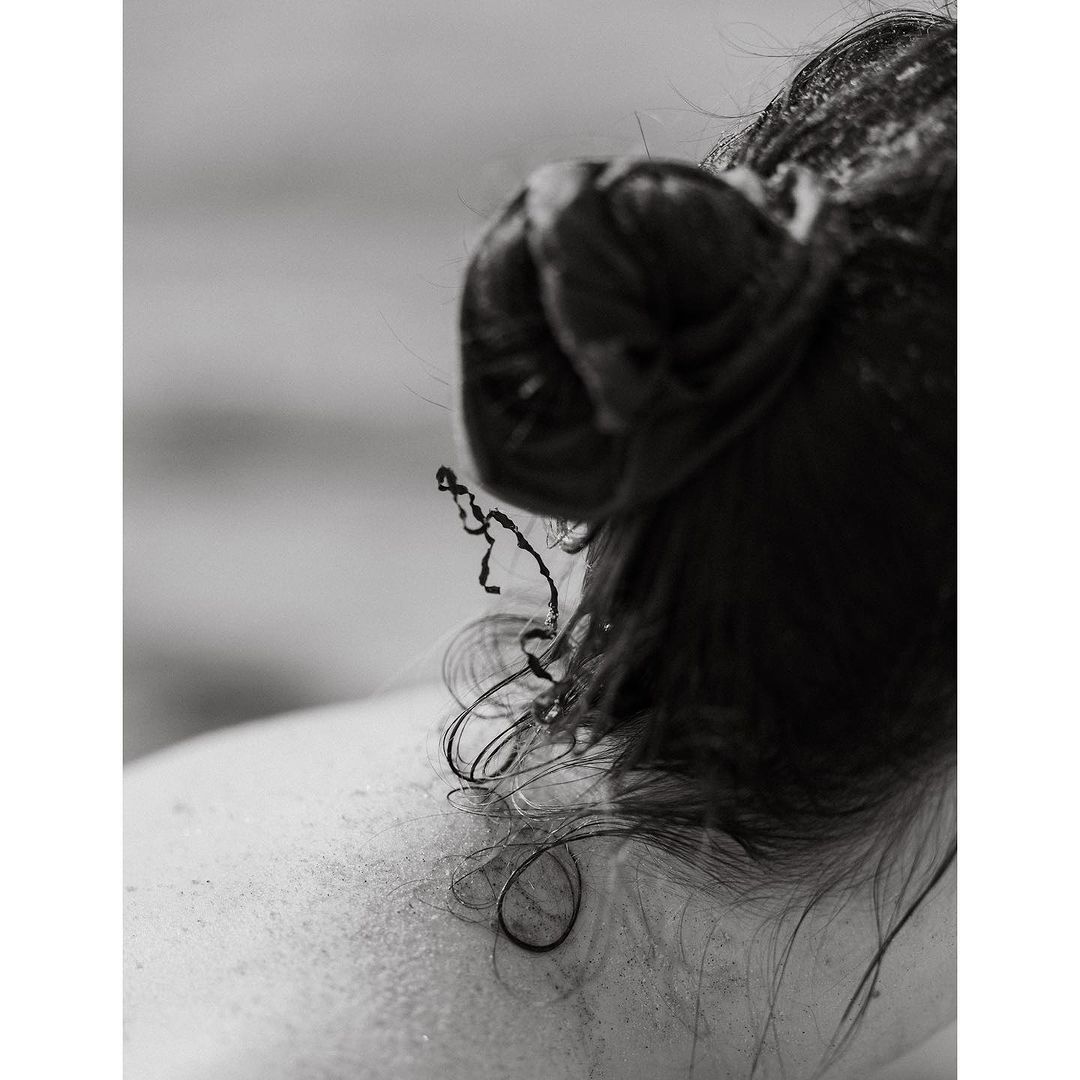 Close-up shot of an adult female's head and upper back. The woman has dark, wet hair pulled back in a messy bun. Monochrome photo.