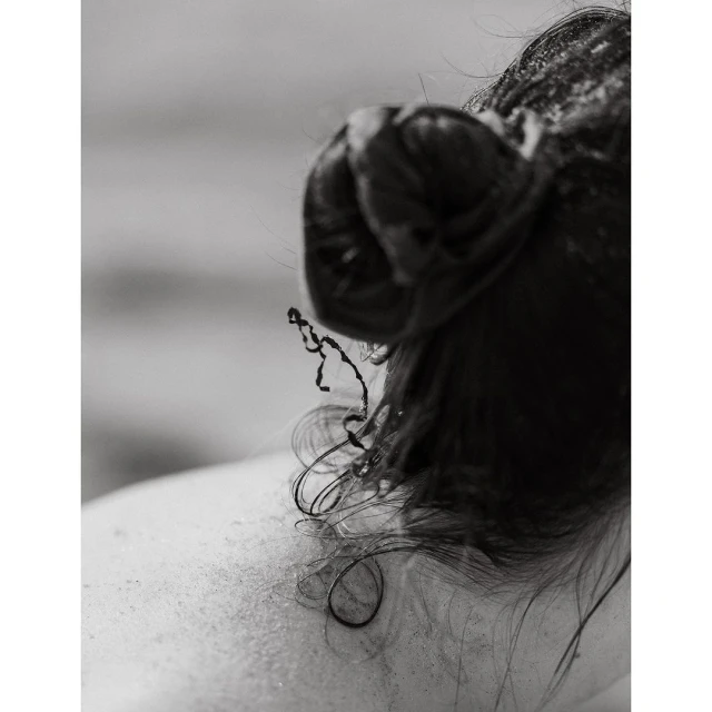 Close-up shot of an adult female's head and upper back. The woman has dark, wet hair pulled back in a messy bun. Monochrome photo.