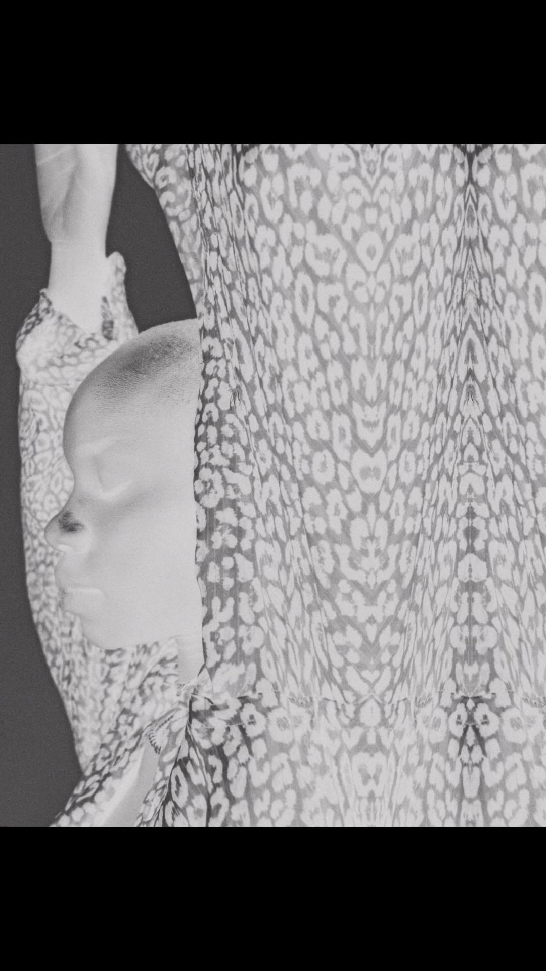 Monochrome portrait of an adult woman with a shaved head partially covered by a leopard-print sheer fabric.