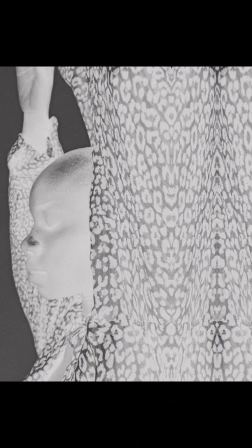 Monochrome portrait of an adult woman with a shaved head partially covered by a leopard-print sheer fabric.