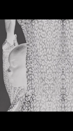 Monochrome portrait of an adult woman with a shaved head partially covered by a leopard-print sheer fabric.