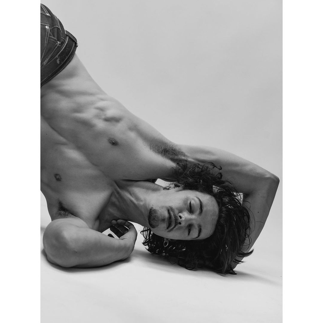 Artistic black and white portrait of a shirtless adult male with closed eyes, laying down with long hair against a plain white background.
