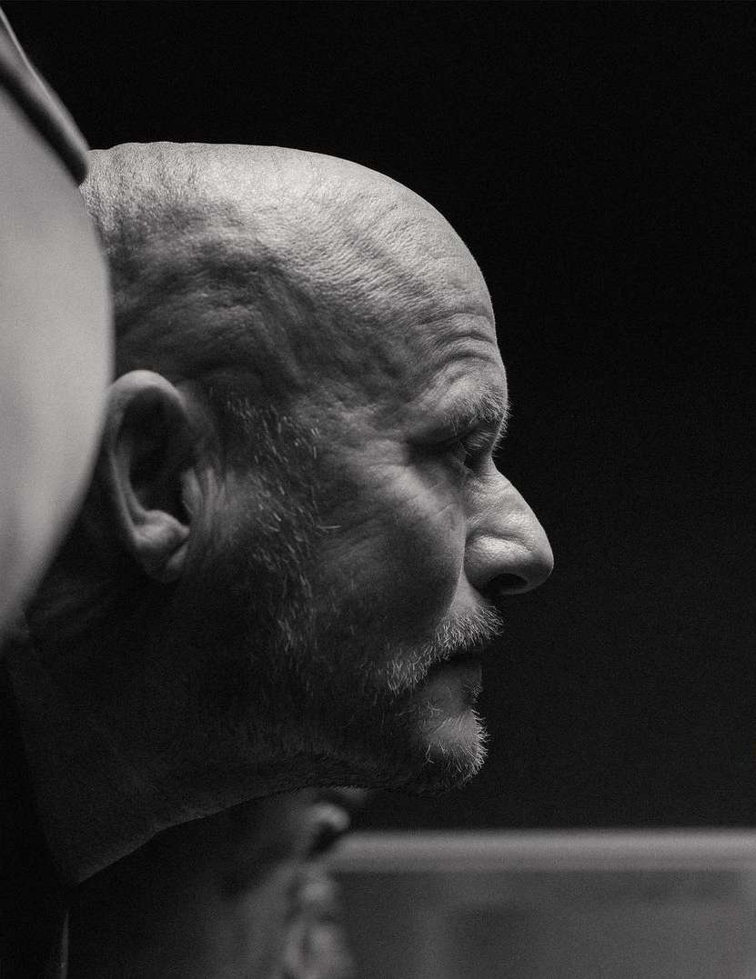 Striking black and white portrait of a mature, bald man in profile, showcasing textured skin and a distinguished beard against a dark backdrop.