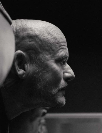 Striking black and white portrait of a mature, bald man in profile, showcasing textured skin and a distinguished beard against a dark backdrop.