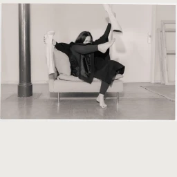 Woman seated on an armchair holding up two tall boots, photographed in Berlin by Ramon Haindl.