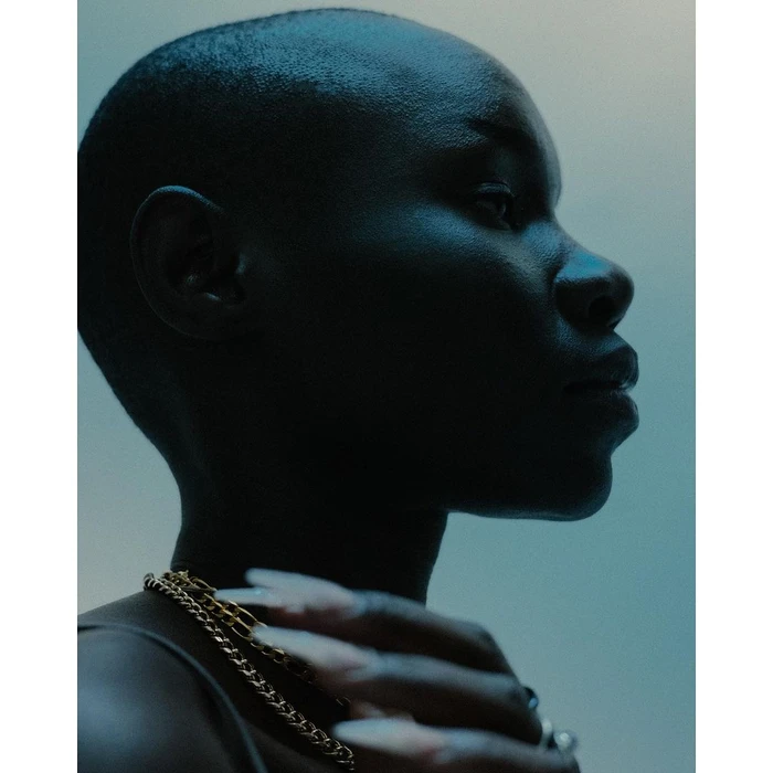 Close-up profile portrait of a person with a shaved head wearing gold chain necklaces, shot by Ramon Haindl.