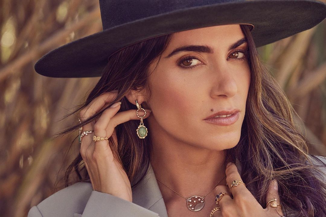 Close-up portrait of a woman wearing a wide-brimmed black hat, statement earrings, and multiple rings, photographed by Ramona Rosales.