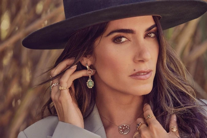 Close-up portrait of a woman wearing a wide-brimmed black hat, statement earrings, and multiple rings, photographed by Ramona Rosales.