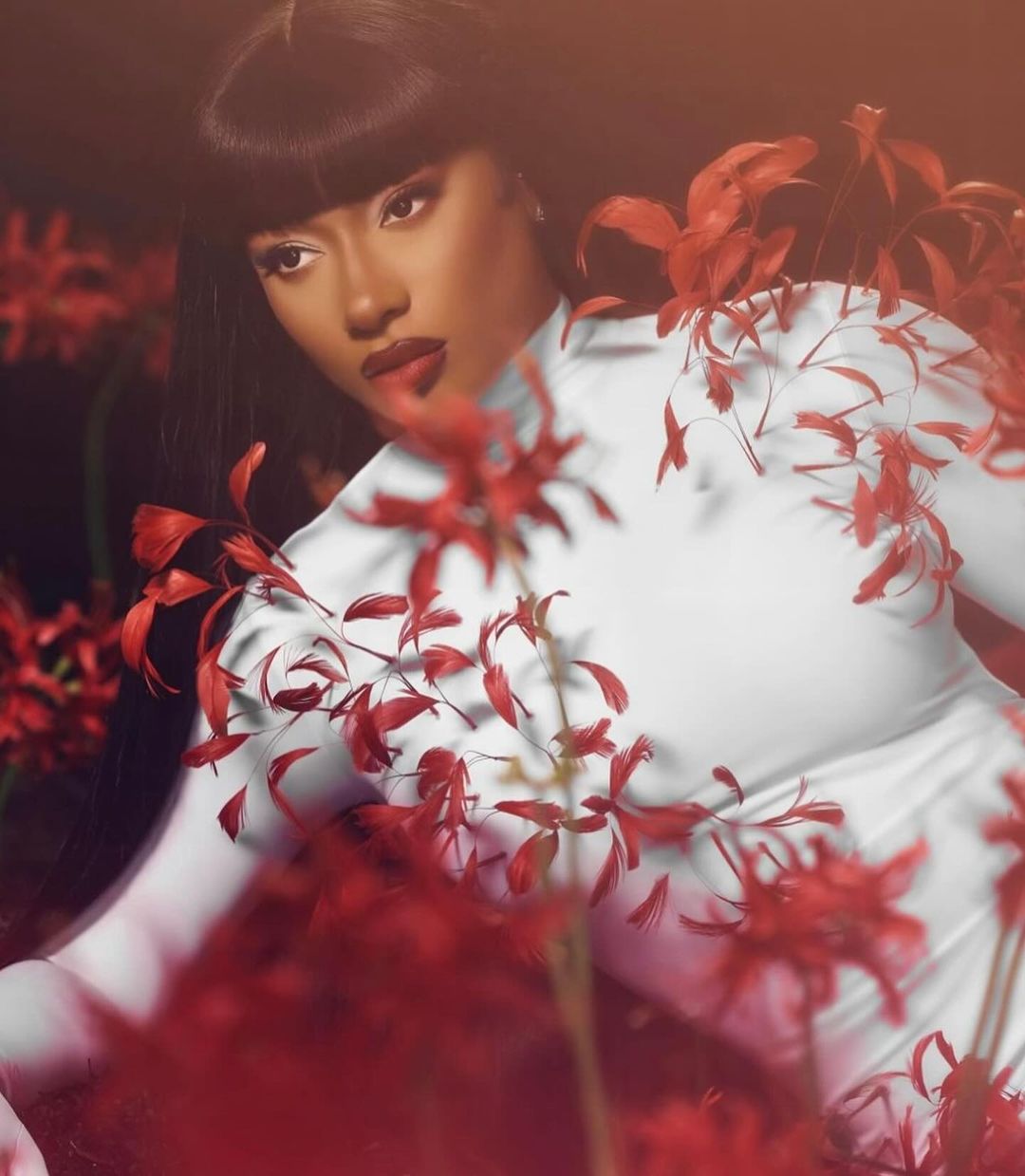 Megan Thee Stallion wearing a white high-neck top surrounded by vibrant red flowers captured by photographer Ramona Rosales