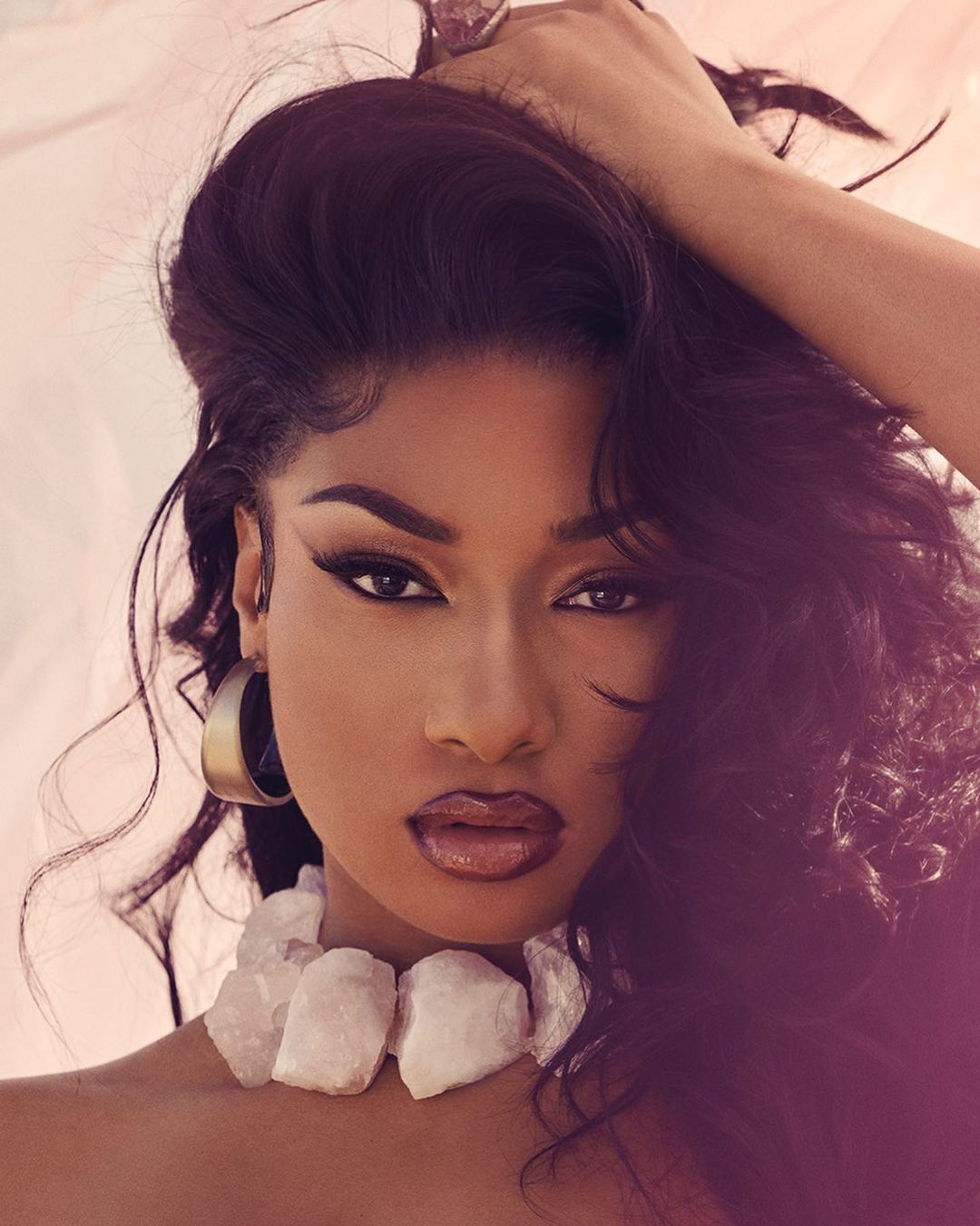 Close-up portrait of a dark-skinned woman with long dark hair posing in a studio with a light background and wearing a chunky white necklace.