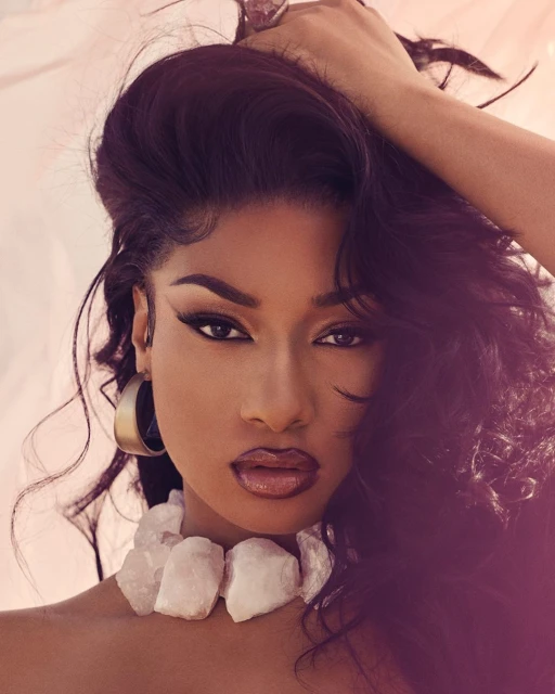 Close-up portrait of a dark-skinned woman with long dark hair posing in a studio with a light background and wearing a chunky white necklace.
