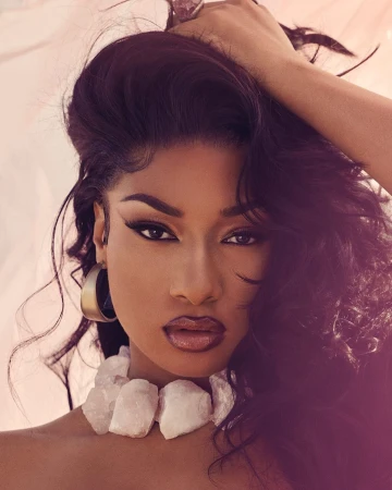 Close-up portrait of a dark-skinned woman with long dark hair posing in a studio with a light background and wearing a chunky white necklace.