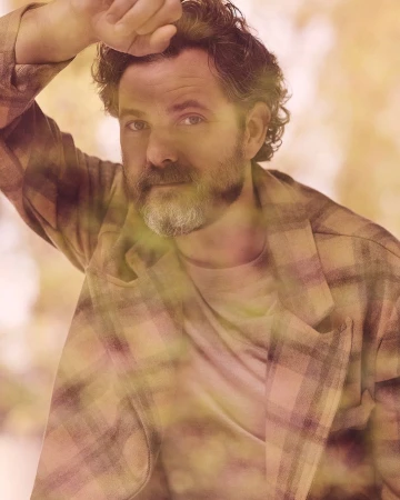 Portrait of a man with curly hair and a beard wearing a plaid jacket, photographed by Ramona Rosales.