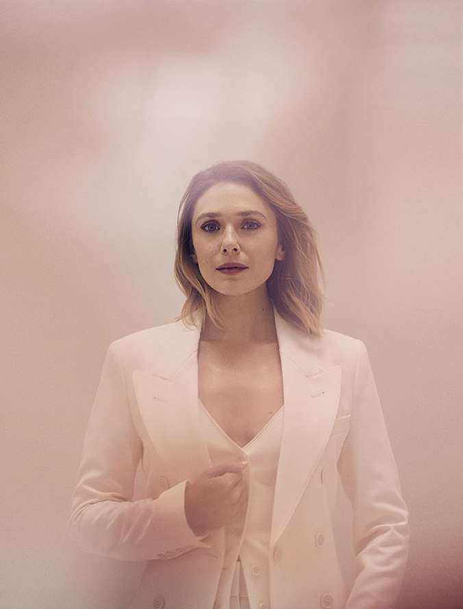 Headshot of fair-skinned adult woman with shoulder-length blonde hair, wearing a white suit, against a pale pink background.