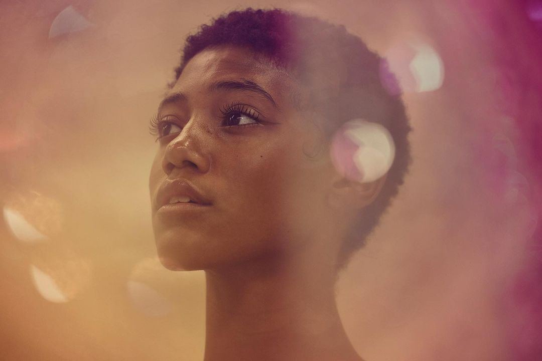 Close-up studio portrait of a young adult woman with short hair looking up; soft golden and pink light create a dreamy effect.