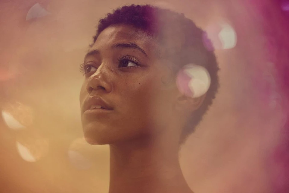 Close-up studio portrait of a young adult woman with short hair looking up; soft golden and pink light create a dreamy effect.