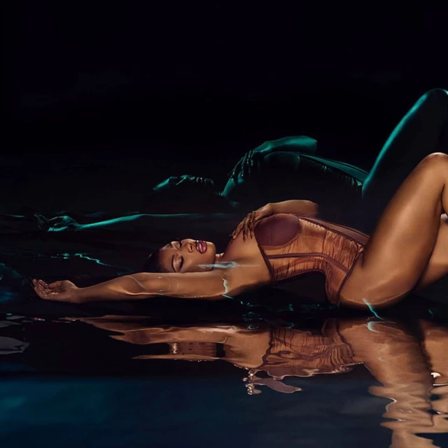 Woman in bronze corset and makeup lying in water with reflection against a dark teal background in a studio shot.